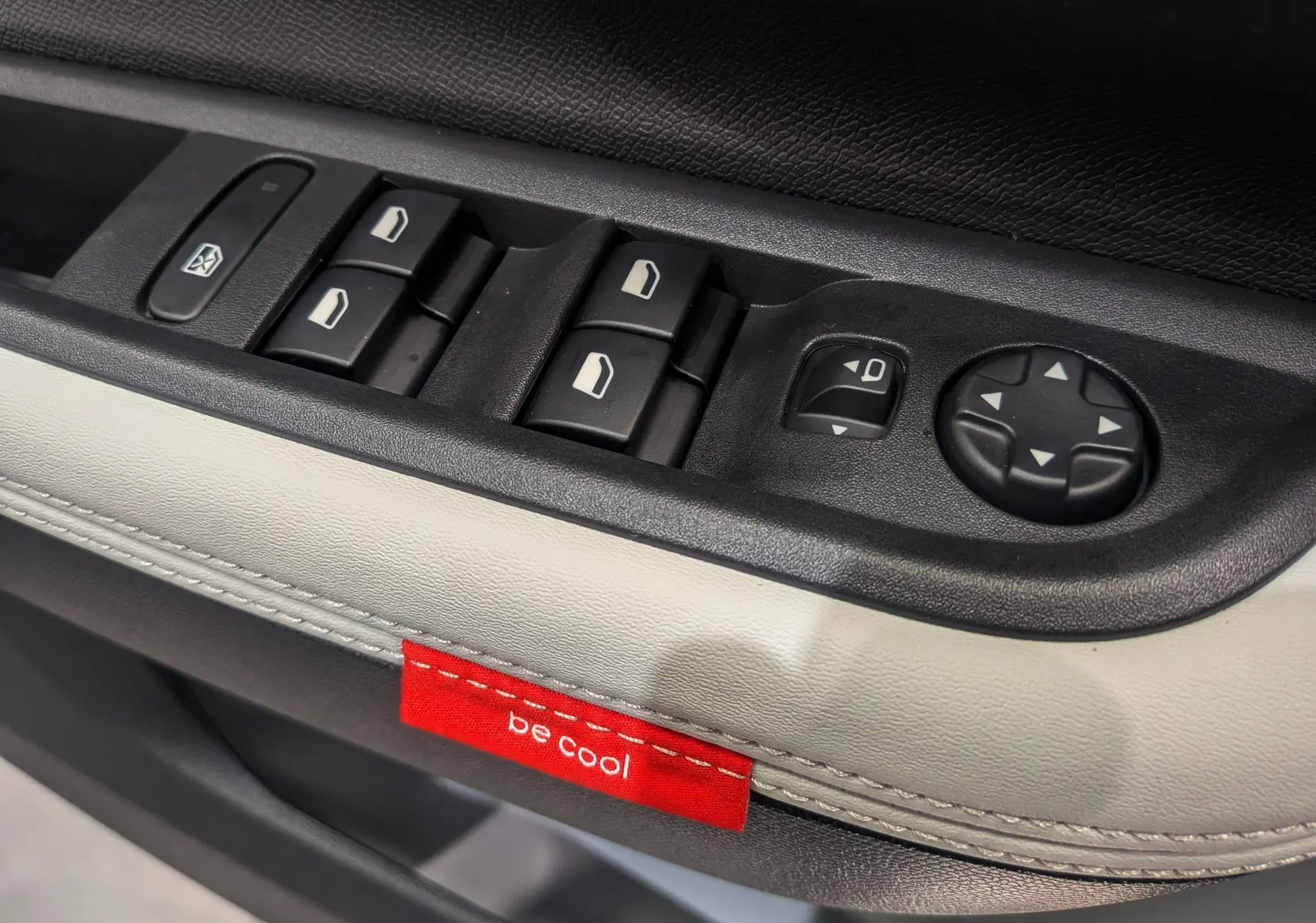 Gros plan sur les commandes de vitres et rétroviseurs côté gauche du Citroën C3 Aircross Hybride 2025 avec étiquette rouge "be cool".