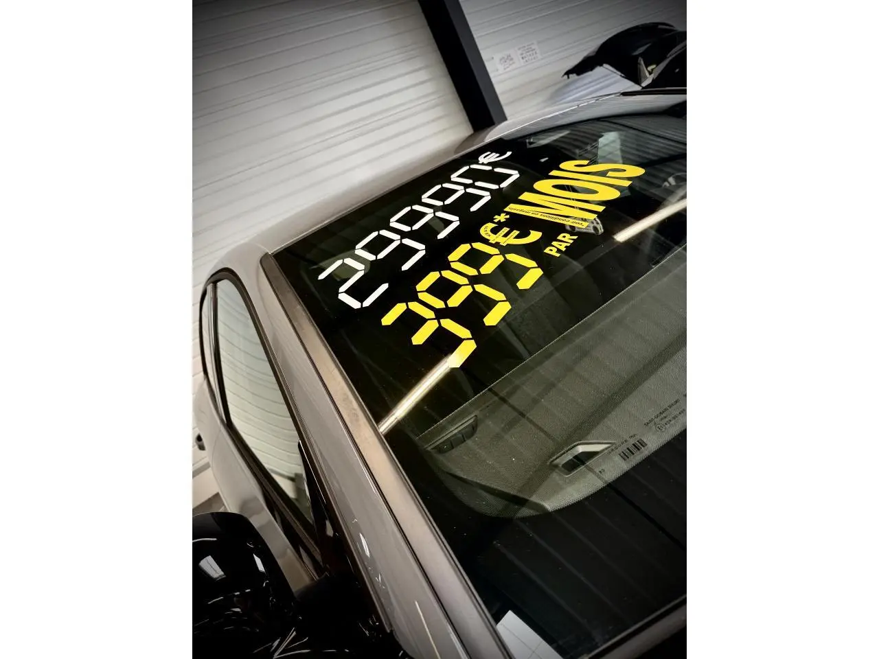 Vue partielle en plongée sur l'avant gauche d'une Peugeot 308 gris selenium avec prix affiché sur le pare-brise.