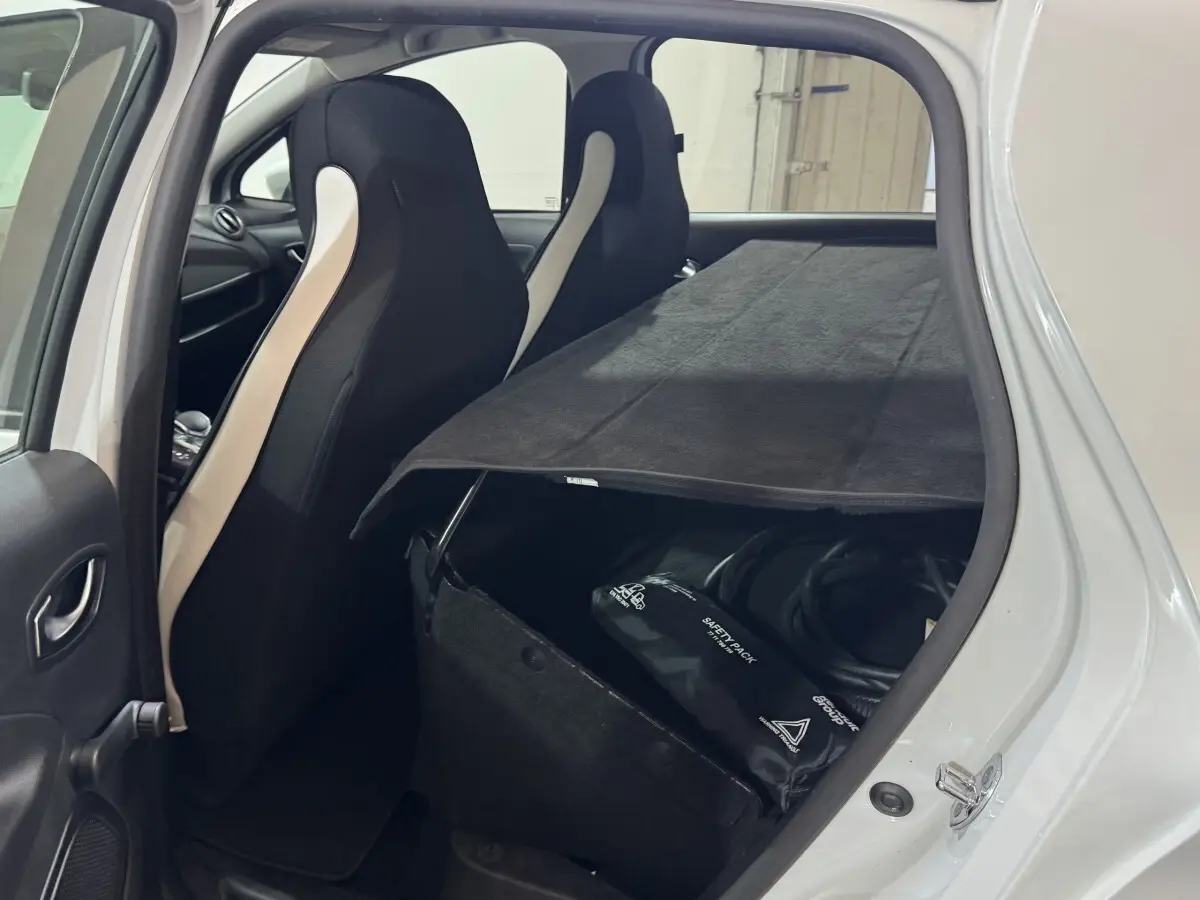 Vue intérieure arrière gauche d'une Renault ZOE blanche 2020, montrant les sièges avant et un rangement avec câble de recharge.