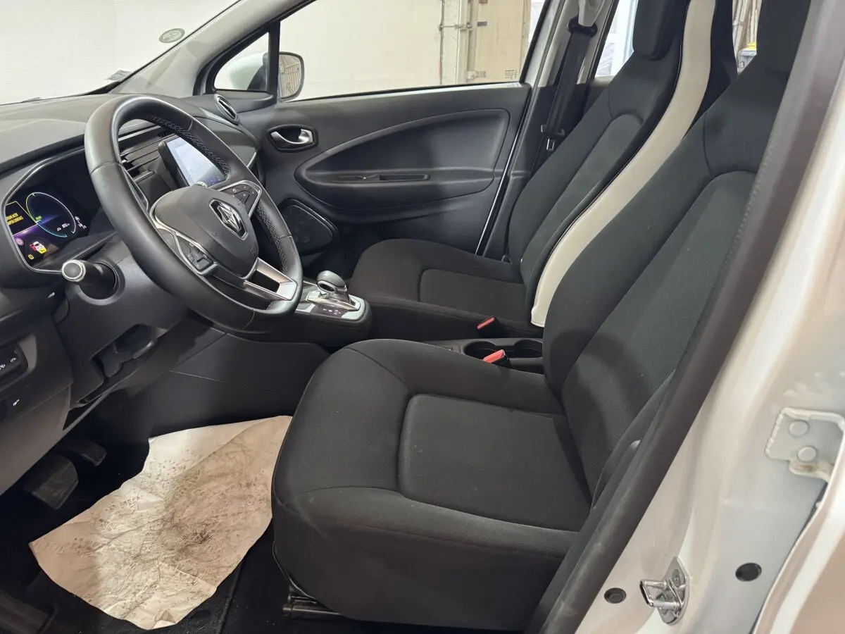 Vue intérieure côté conducteur de la Renault ZOE Business 2020 blanche, avec sièges noirs et volant multifonctions.