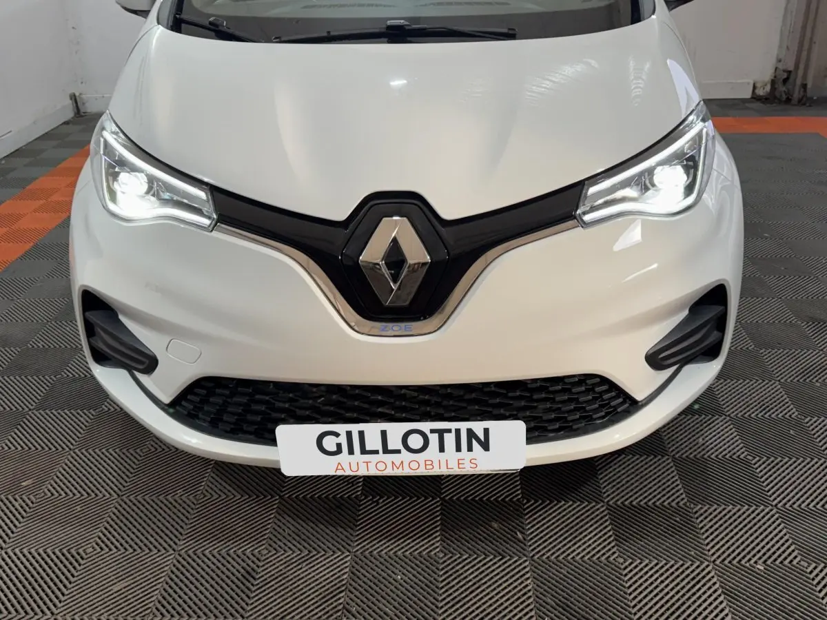 Vue frontale rapprochée de la Renault ZOE Business blanche avec phares LED allumés et logo Renault bien visible.