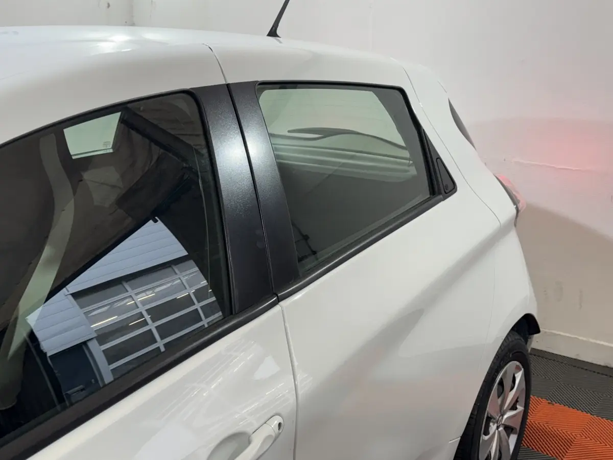 Vue côté gauche arrière d'une Renault ZOE Business blanche, mettant en valeur la vitre arrière et la poignée de porte.
