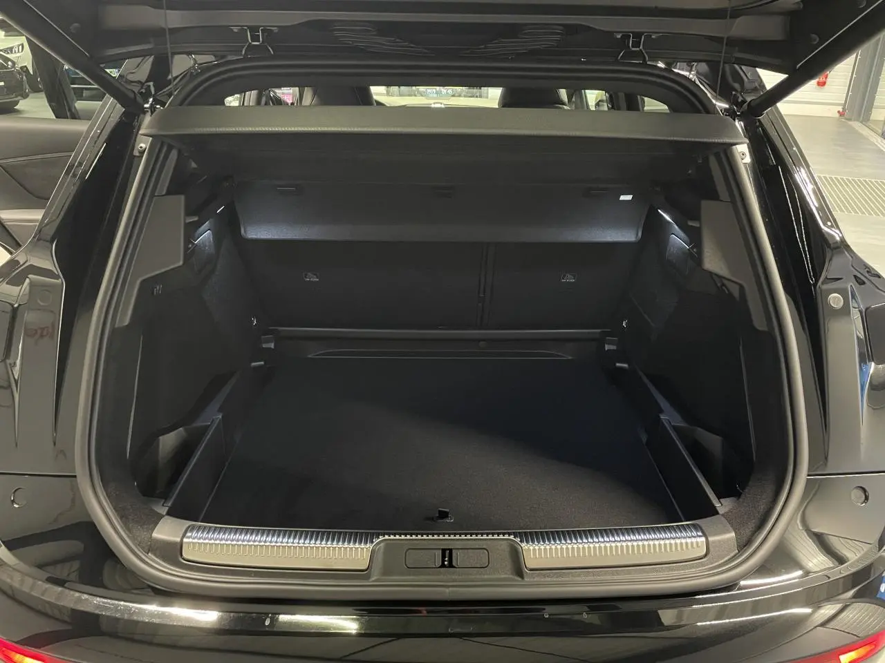Vue arrière du coffre ouvert du DS7 Crossback noir métallisé, mettant en valeur l'espace de chargement et la finition soignée.