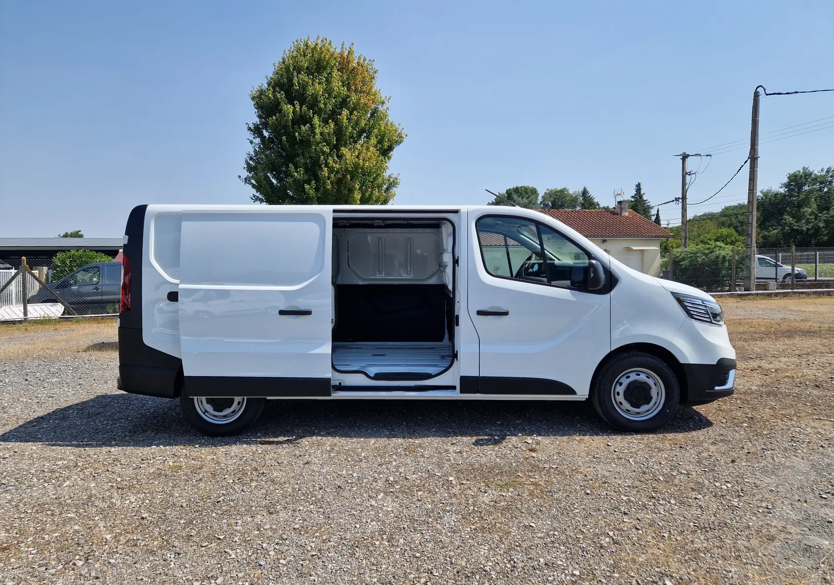 Vue de profil côté droit d’un Renault Trafic Fourgon blanc 2026 avec porte latérale coulissante ouverte montrant l’espace de chargement.