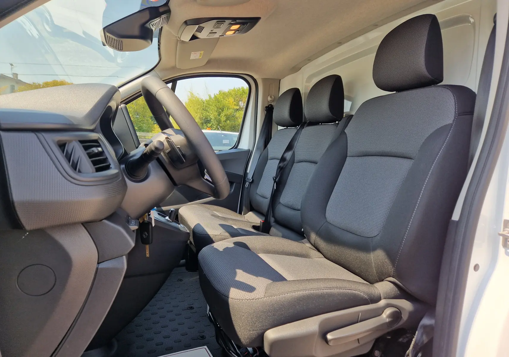 Vue intérieure côté conducteur du Renault Trafic Fourgon blanc 2026, montrant les sièges avant en tissu gris et tableau de bord.