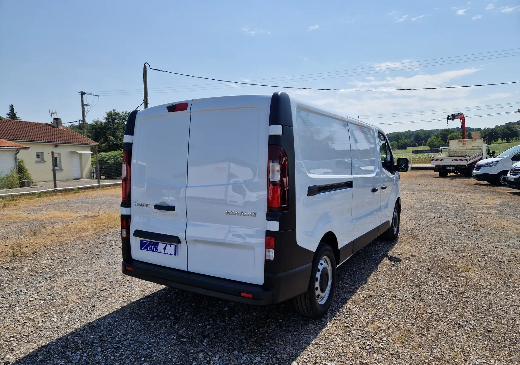 Renault Trafic Fourgon blanc vu en 3/4 arrière droit sur un terrain gravillonné par temps ensoleillé.