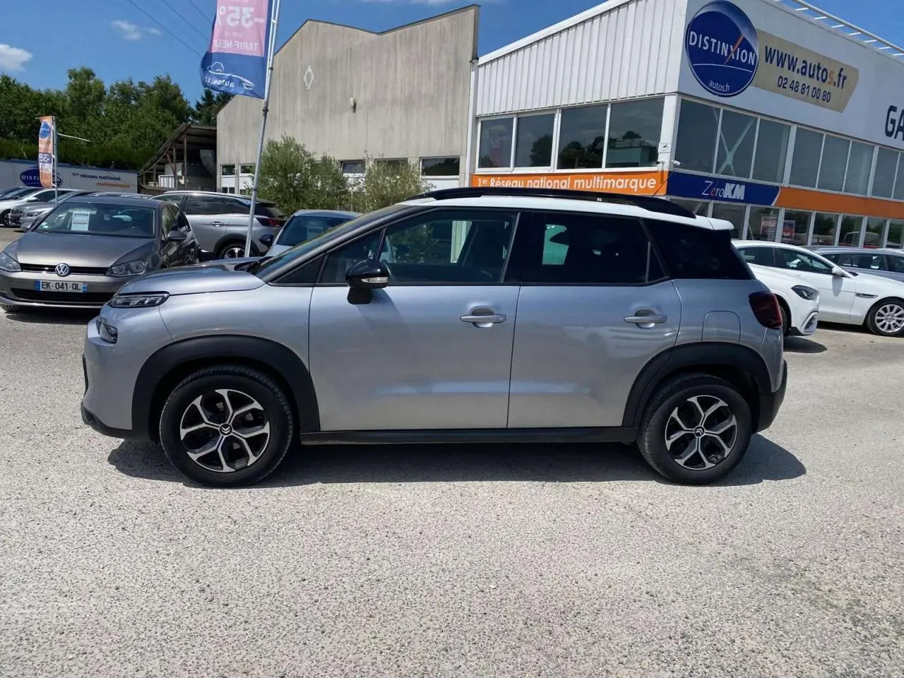 Profil côté gauche d'un Citroën C3 Aircross gris Artense avec toit blanc, garé devant un concessionnaire en extérieur.