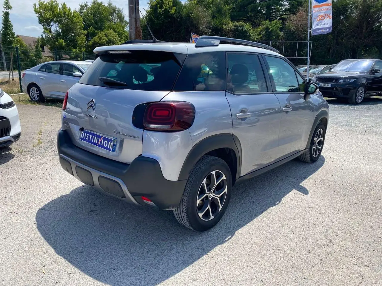 Vue 3/4 arrière droite d'un Citroën C3 Aircross gris Artense avec toit blanc, feux arrière distinctifs et jantes noires.