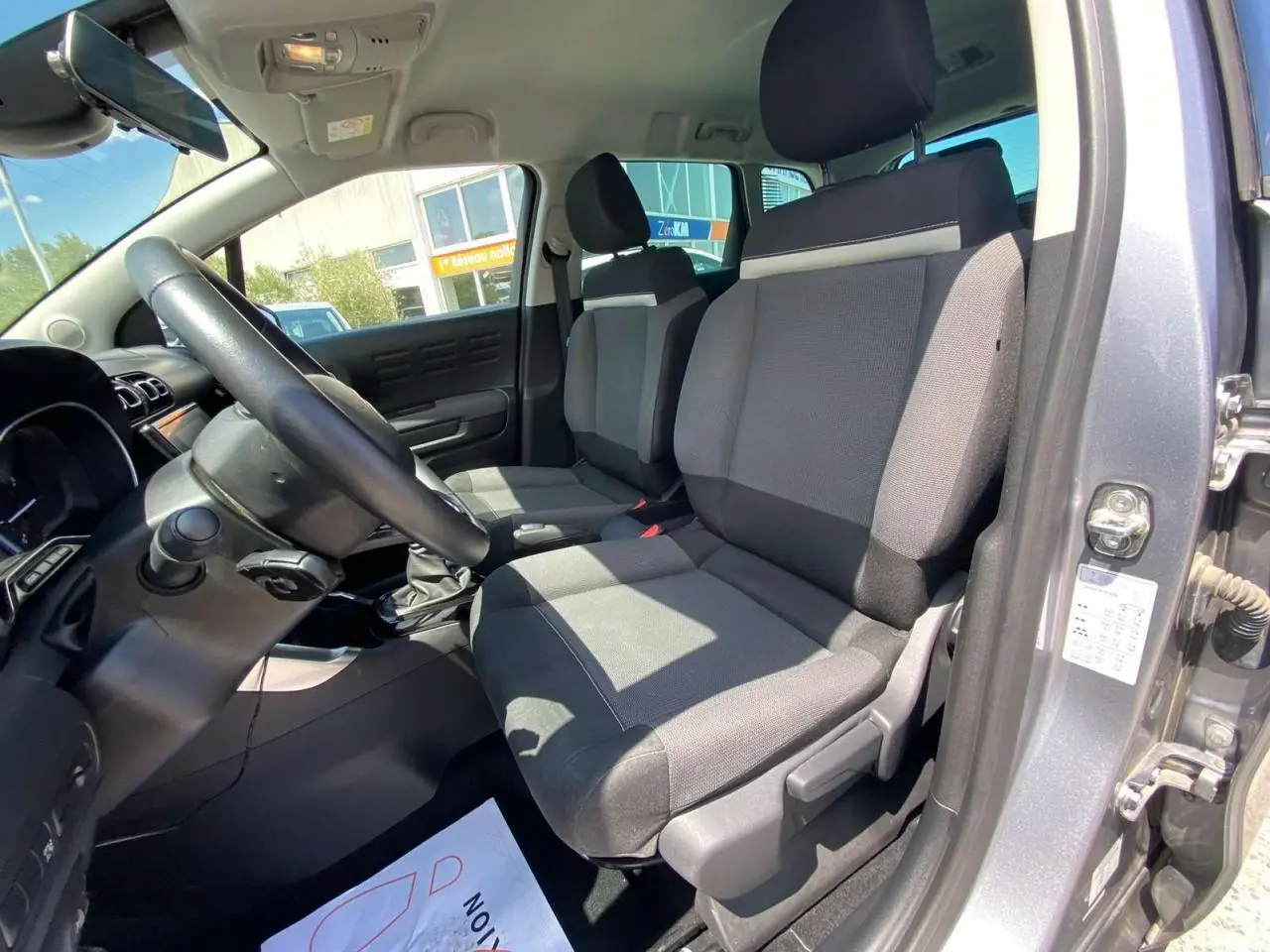 Intérieur avant droit du Citroën C3 Aircross gris Artense, sièges tissu bicolore et volant noir visible.