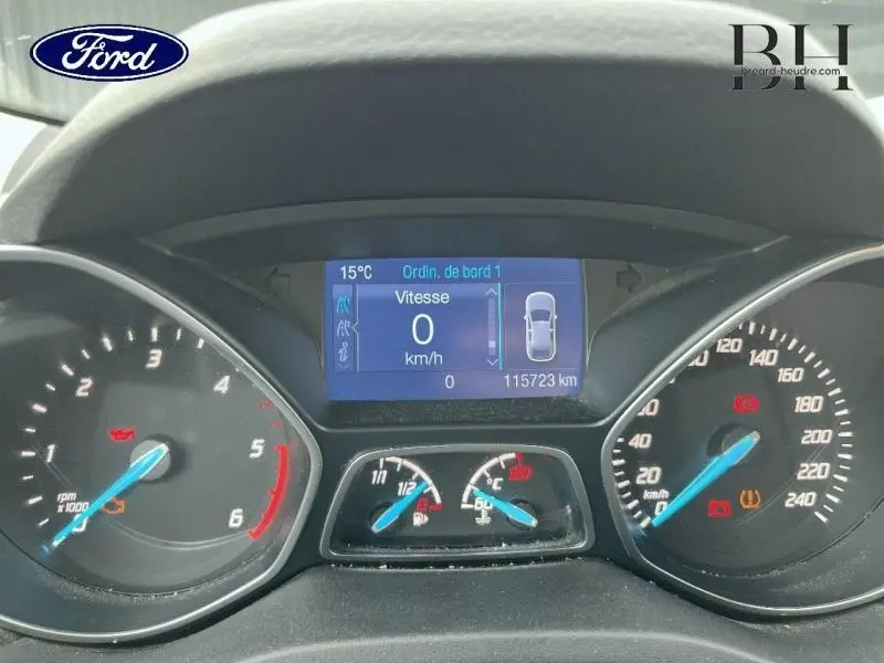 Vue rapprochée du tableau de bord numérique du Ford Kuga gris, affichant vitesse à 0 km/h et 115723 km au compteur.