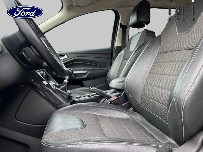 Vue intérieure côté conducteur du Ford Kuga 2015 avec sièges cuir/tissu noir et volant multifonction en cuir.