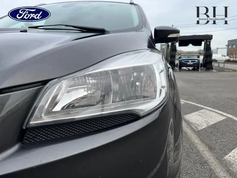 Gros plan sur le phare avant droit d'un Ford Kuga 2.0 TDCi 150ch Titanium gris Magnetic, avec rétroviseur noir visible.