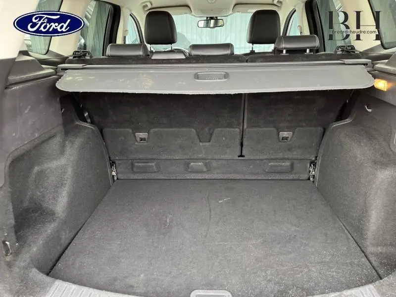 Coffre spacieux du Ford Kuga gris Magnetic vu de l'arrière avec cache-bagages et sièges arrière en cuir noir visibles.