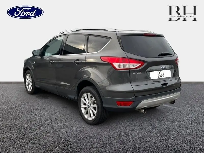 Ford Kuga gris Magnetic vu en 3/4 arrière droit, avec jantes alu et sorties d’échappement chromées visibles.