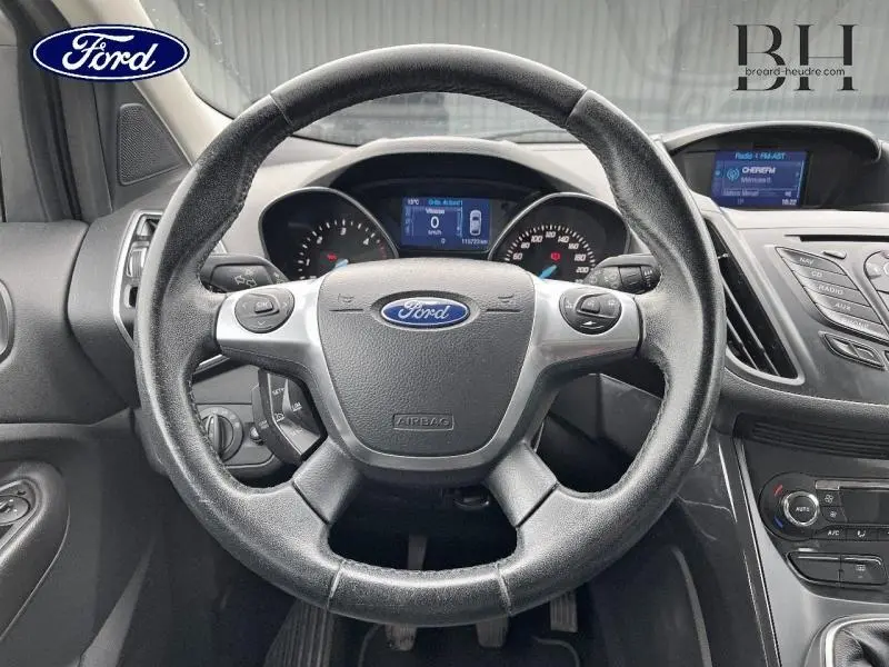 Vue rapprochée du volant cuir multifonction d'un Ford Kuga 2015, avec tableau de bord et écran tactile visibles.