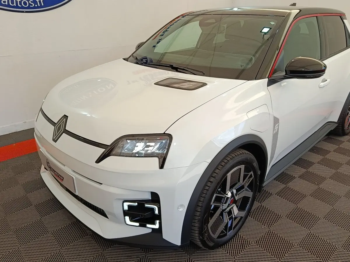 Vue 3/4 avant droite d'une Renault R5 Techno électrique blanche avec détails noirs et toit contrasté rouge.