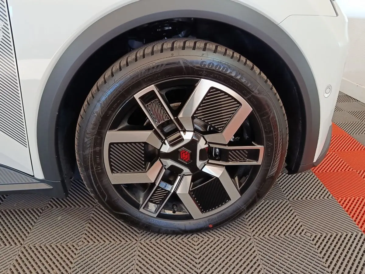 Gros plan sur la roue avant droite d'une Renault R5 Techno blanche, jante noire et argentée au design moderne.