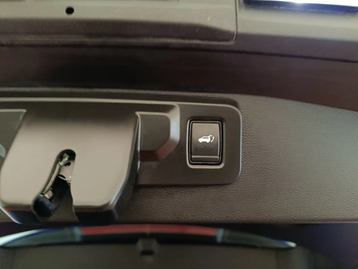 Bouton d'ouverture électrique du coffre sur panneau intérieur noir du Renault Symbioz bleu, vue rapprochée.