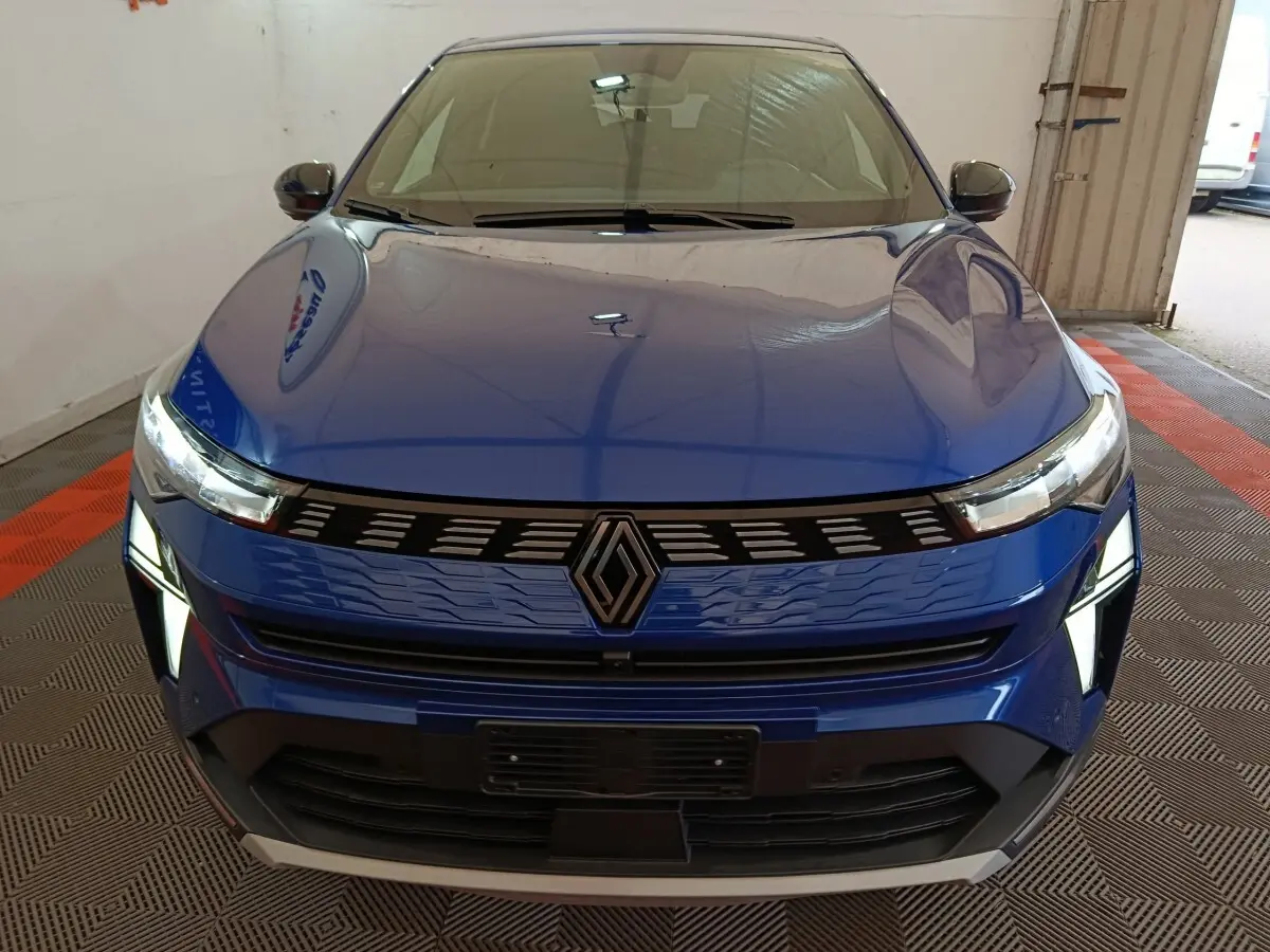 Vue frontale d’une Renault Symbioz bleu électrique avec calandre noire et phares LED allumés dans un garage.