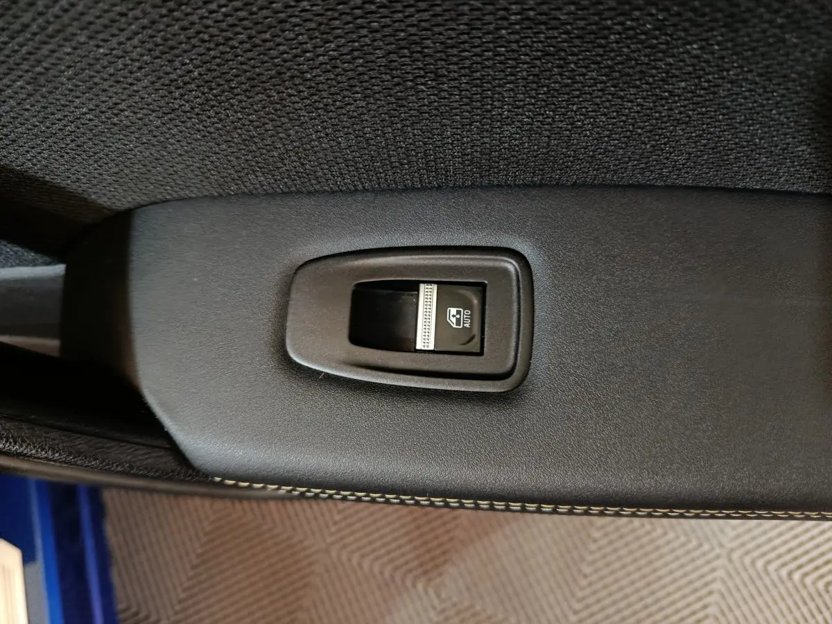 Gros plan sur l'interrupteur de lève-vitre électrique noir dans l'habitacle du Renault Symbioz bleu.