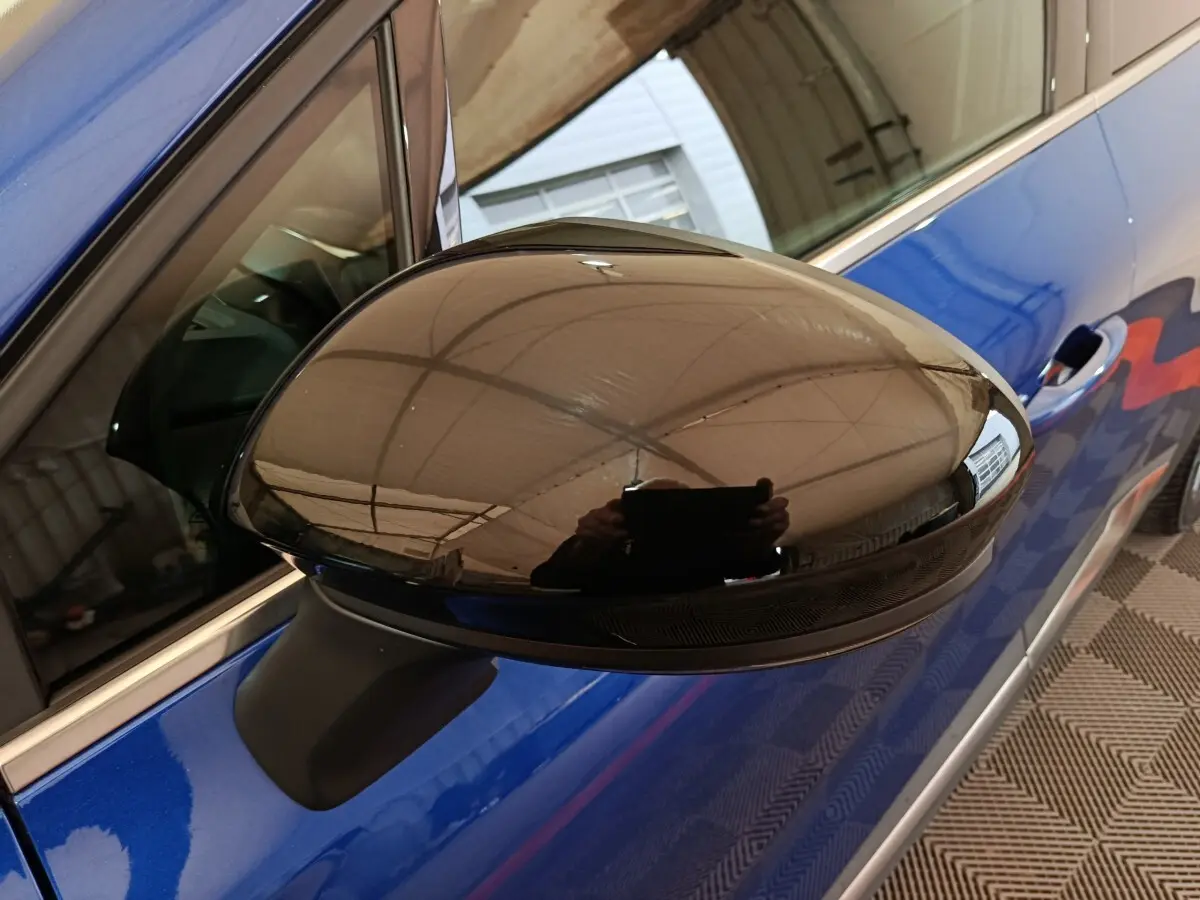 Rétroviseur noir brillant côté gauche sur Renault Symbioz bleu, vue rapprochée en angle avant.