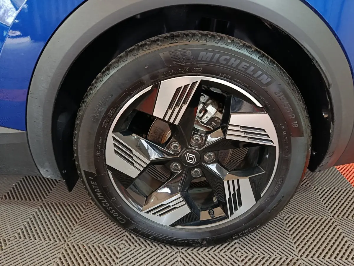 Gros plan sur la roue avant droite bleue du Renault Symbioz 2025 avec jante noire et argent au design géométrique.