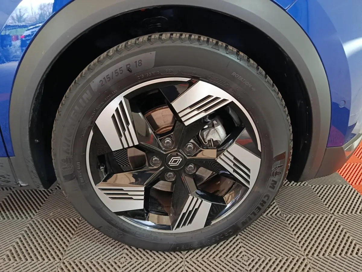 Gros plan sur la roue avant droite bleu Renault Symbioz 2025 avec jante noire et argent au design géométrique.