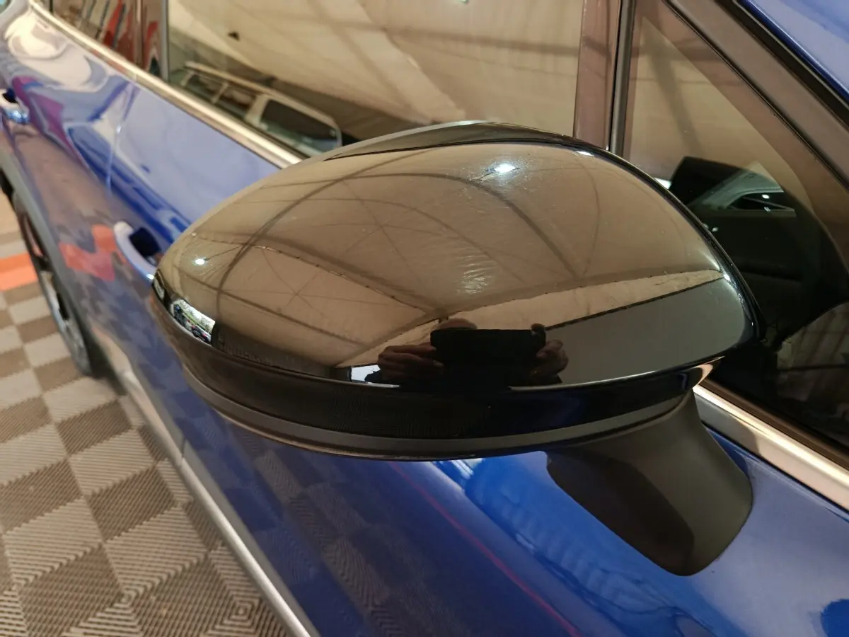 Gros plan sur le rétroviseur noir côté gauche d'une Renault Symbioz bleu électrique, avec reflet intérieur visible.