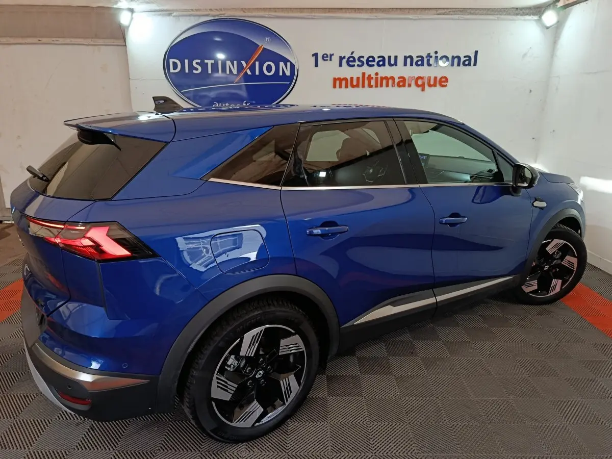 Vue 3/4 arrière droite d’un Renault Symbioz bleu électrique avec jantes noires et feux arrière LED allumés dans un showroom.