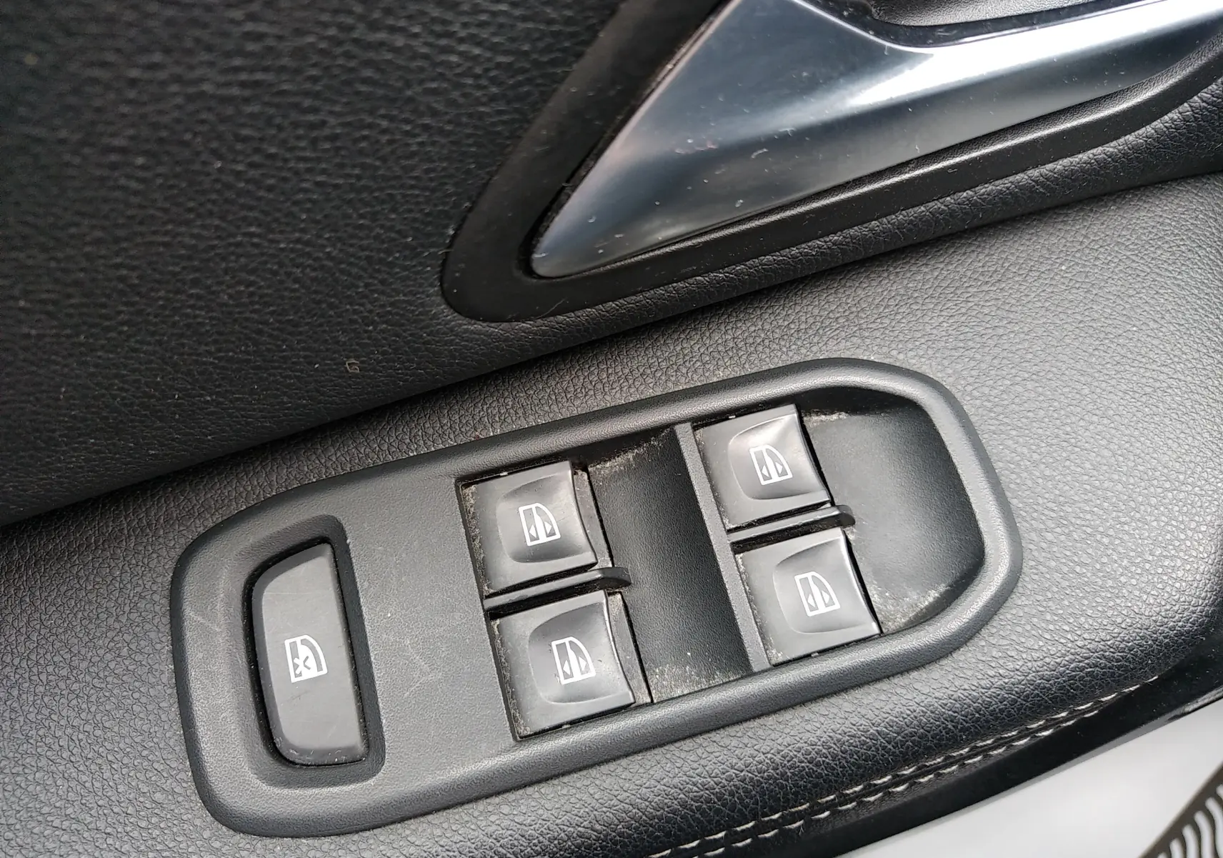 Gros plan sur les commandes de lève-vitres électriques côté conducteur du Dacia Duster gris 2020, finition Prestige.