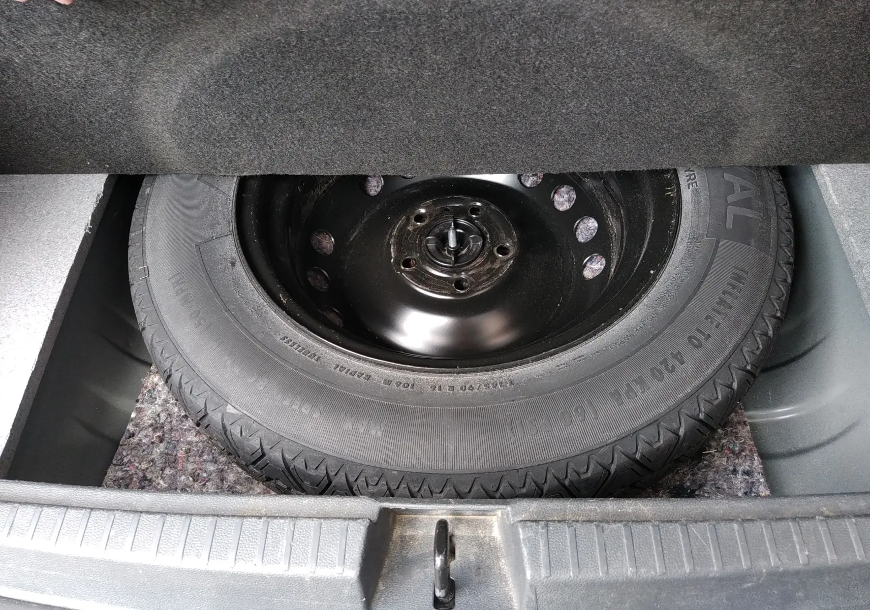 Vue rapprochée de la roue de secours noire dans le coffre d'un Dacia Duster gris 2020, version Prestige.