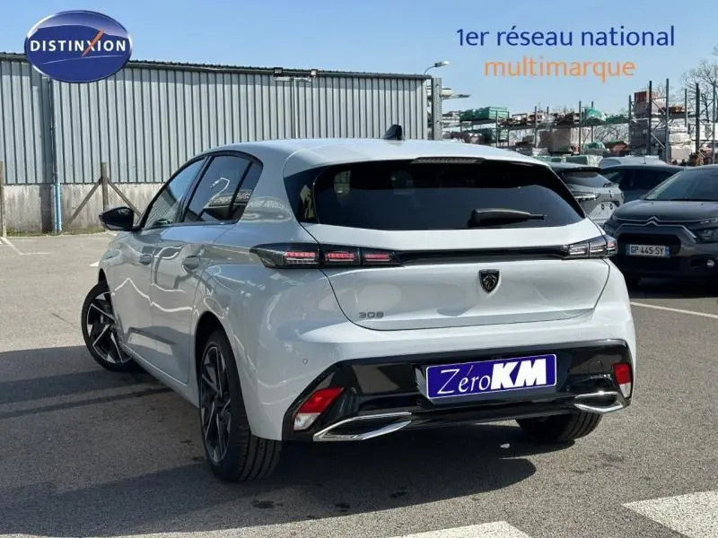 Vue 3/4 arrière d'une Peugeot 308 blanche avec feux arrière LED et jantes alliage noires sur parking.