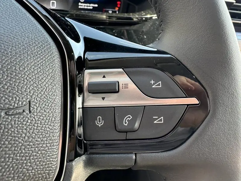 Gros plan sur les commandes multifonctions noires et argentées du volant côté gauche d'une Peugeot 308 bleu 2025.