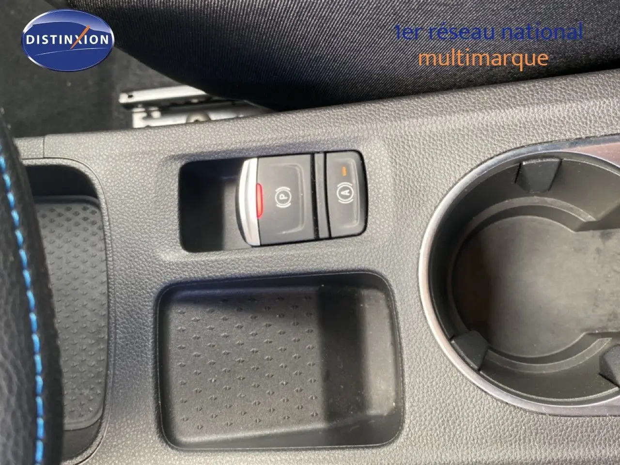 Gros plan sur la console centrale noire avec boutons de frein à main électronique et maintien auto, et porte-gobelet circulaire.