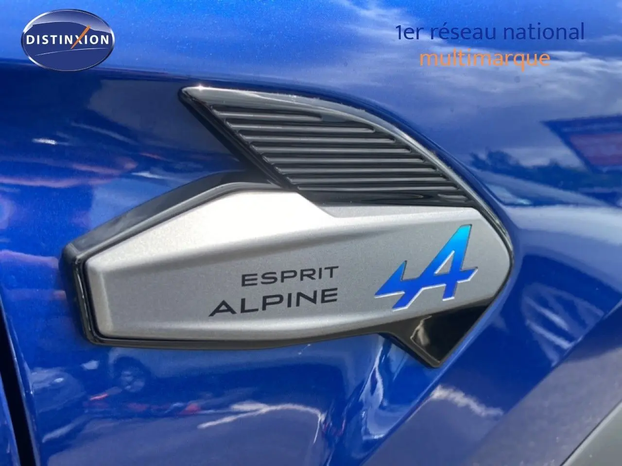 Gros plan sur l'emblème Esprit Alpine bleu sur la carrosserie bleu iron metal d'une Renault Symbioz hybride.