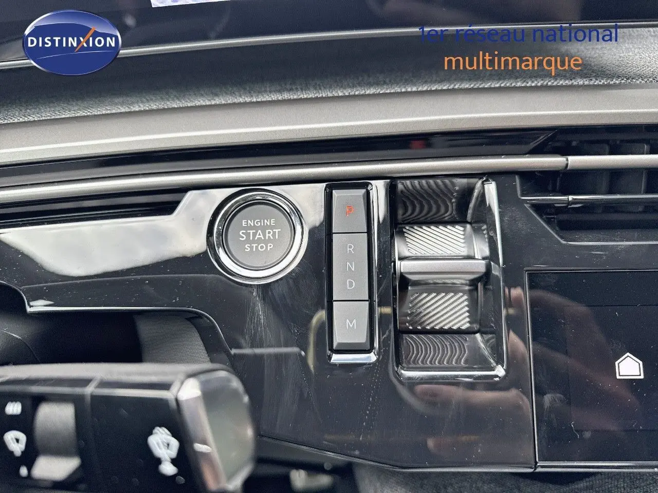 Gros plan sur la console centrale noire brillante du Peugeot 3008 Hybrid 2025 avec bouton start/stop et commandes de boîte auto.