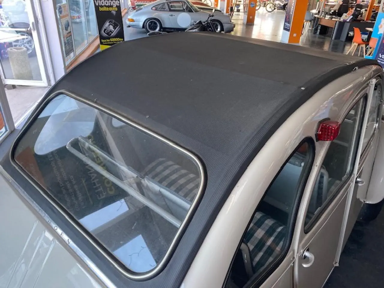 Vue 3/4 arrière droite d'une Citroën 2 CV beige clair de 1968 rénovée, avec toit ouvrant en toile noire et feux arrière rouges.