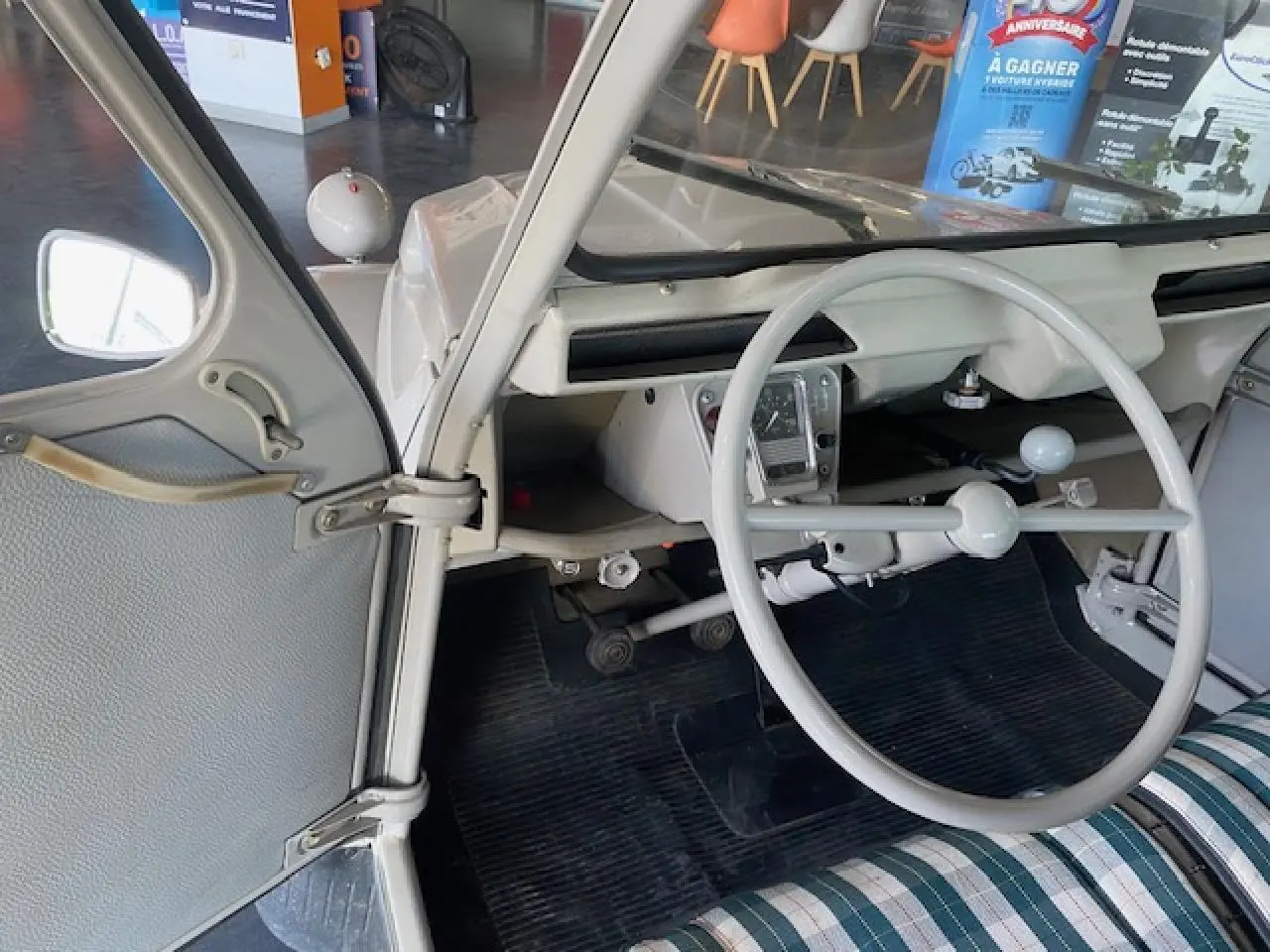 Vue intérieure côté gauche de la Citroën 2 CV beige clair de 1968, volant fin et tableau de bord minimaliste.