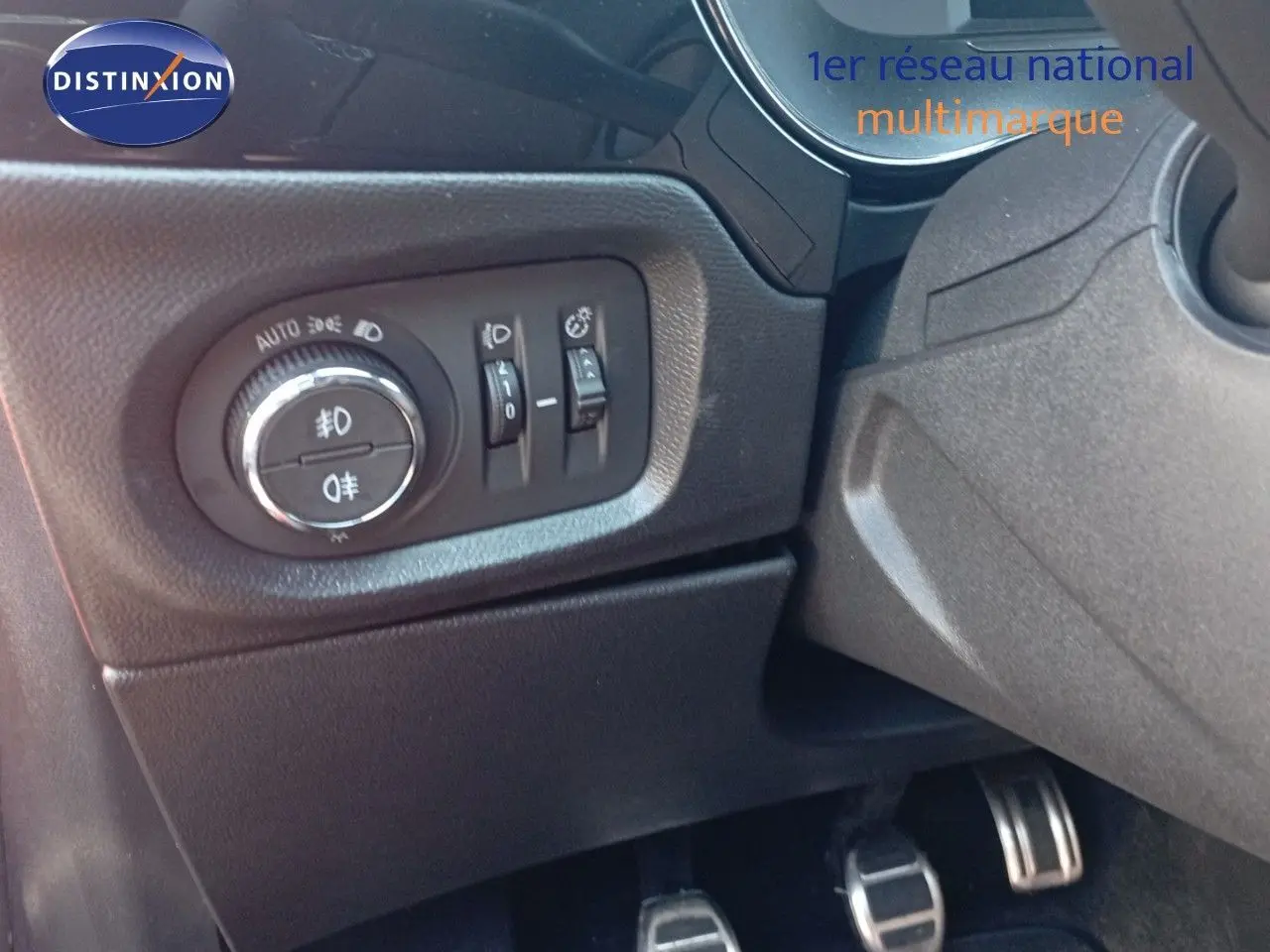 Détail du tableau de bord côté gauche avec commandes d'éclairage et pédales d'une Opel Corsa rouge 2023.