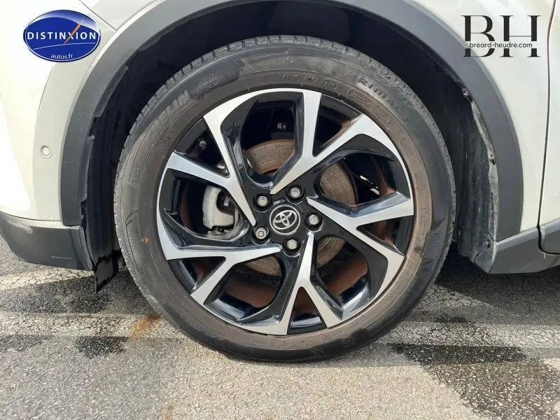 Gros plan sur la roue avant gauche du Toyota C-HR blanc nacré bi-ton avec jante alu noire et argentée.
