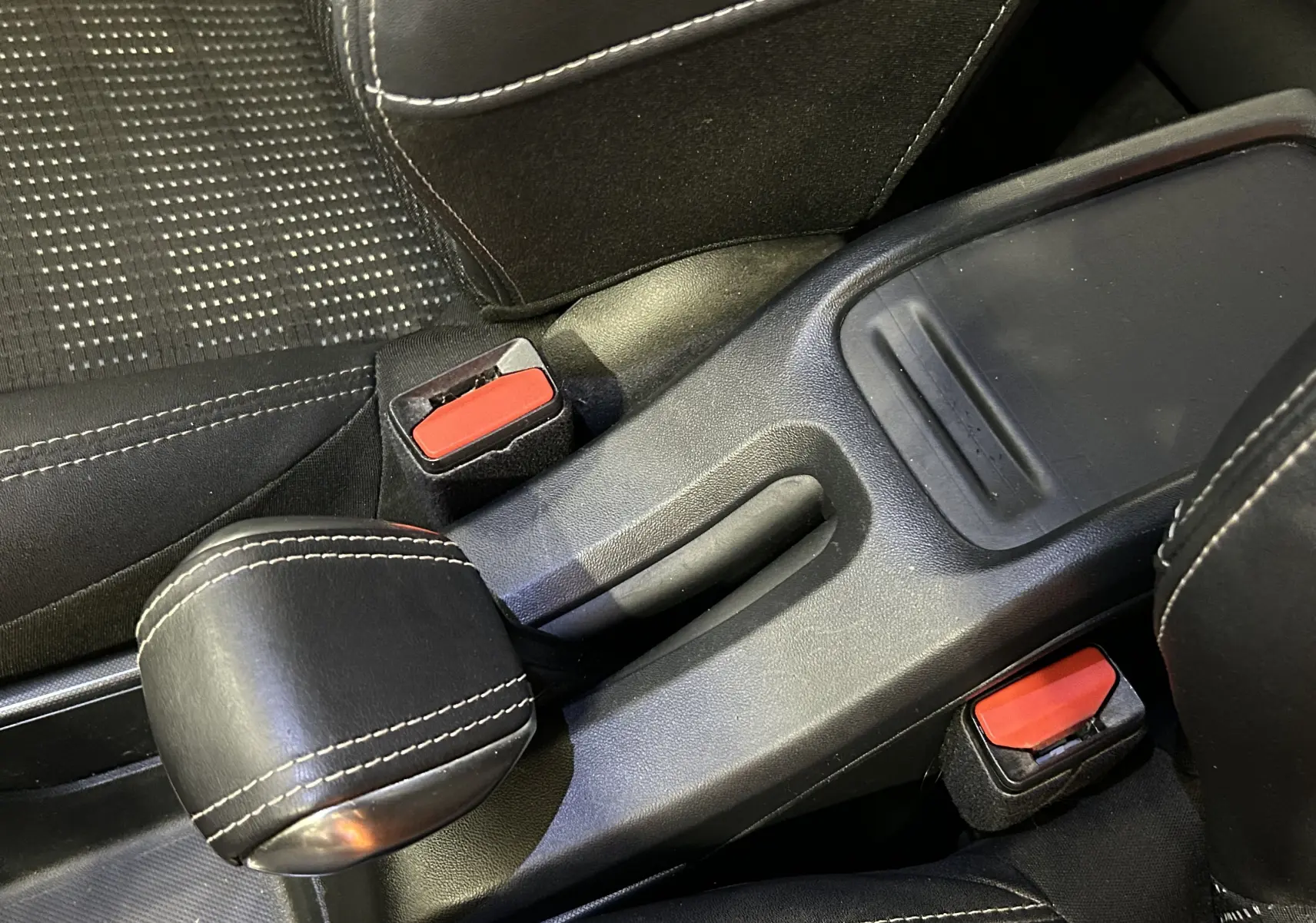 Gros plan sur le frein à main en cuir noir et les boucles de ceinture rouge dans l'habitacle d'une Peugeot 2008 blanche.