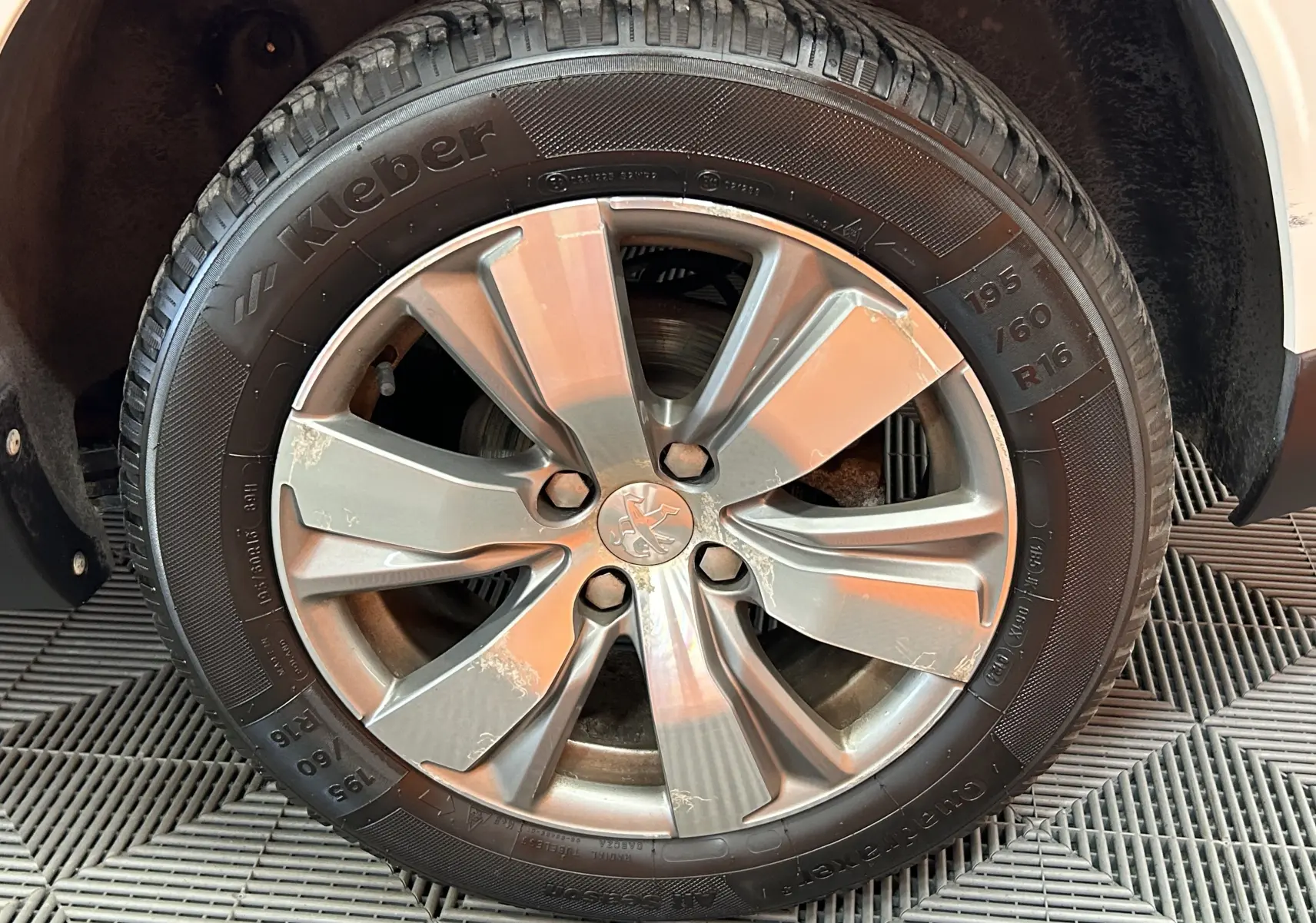 Gros plan sur la roue avant droite d’un Peugeot 2008 blanc, jante alliage grise avec traces d’usure visibles.