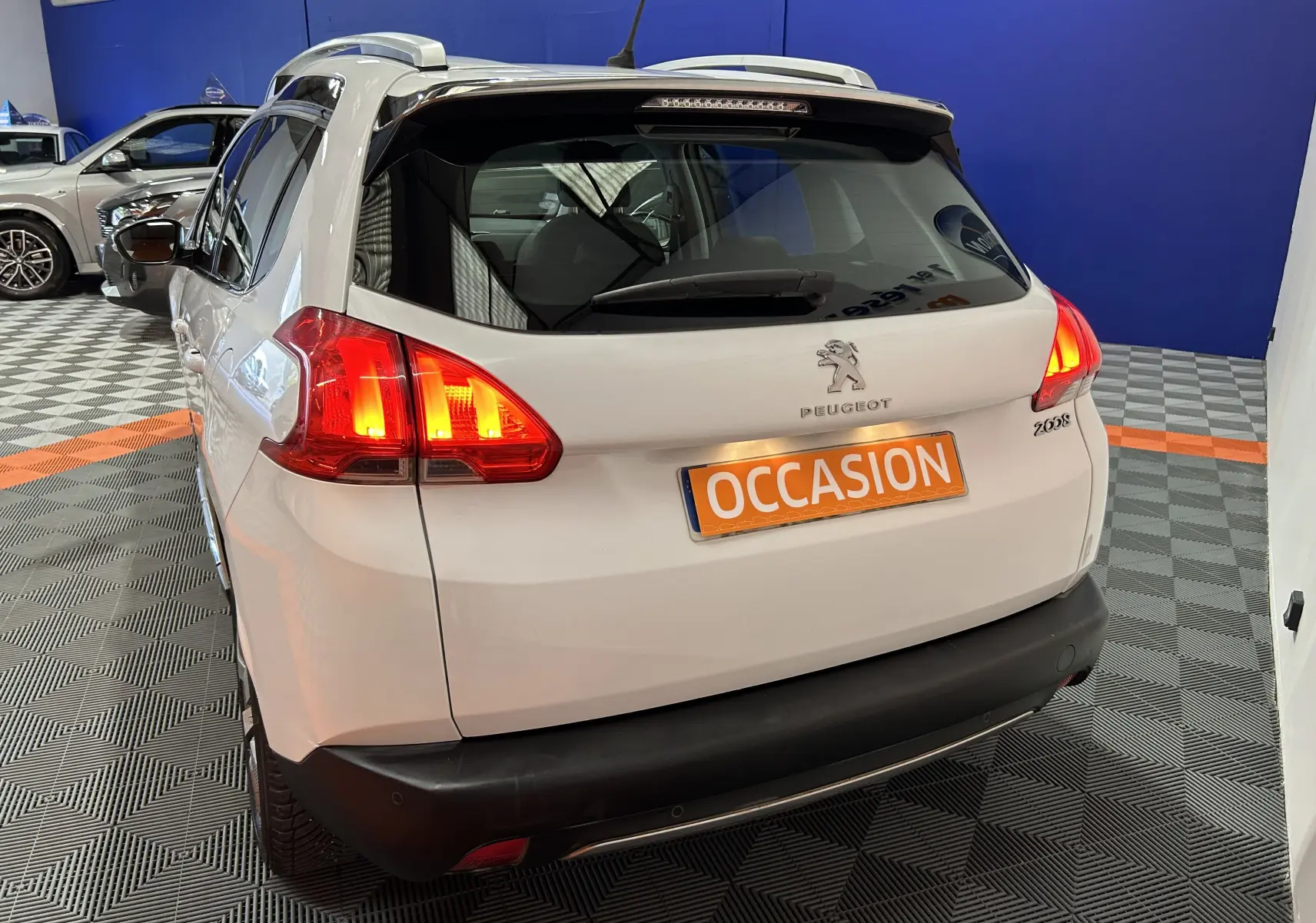 Vue 3/4 arrière droite d’un Peugeot 2008 blanc avec feux arrière allumés et plaque d’immatriculation "OCCASION" visible.