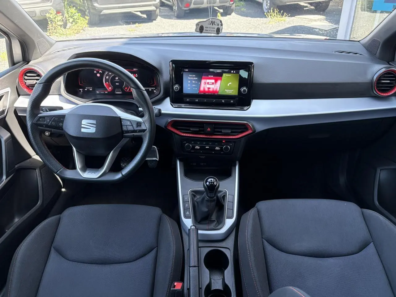 Vue intérieure avant du tableau de bord et volant cuir de la SEAT Arona 2024 avec écran tactile et détails rouges sur aérateurs.