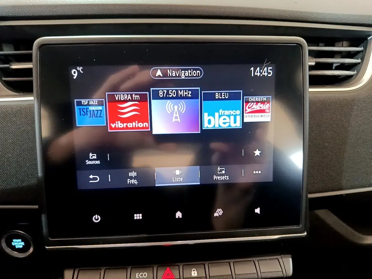 Écran tactile central de la Renault ZOE Business R110 blanc, affichant les stations radio avec bouton démarrage visible à gauche.