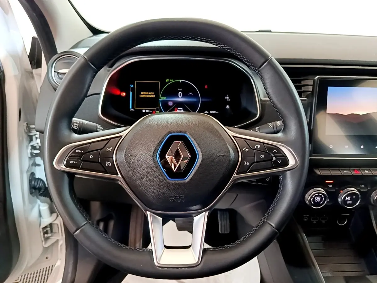 Vue intérieure centrée sur le volant cuir noir de la Renault ZOE blanc, avec tableau de bord digital et écran tactile visible.