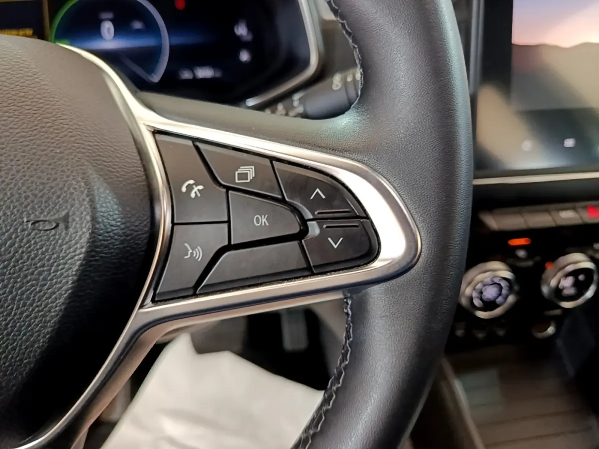 Gros plan sur les commandes multifonctions côté droit du volant cuir noir de la Renault ZOE blanche, tableau de bord en arrière-plan flou.