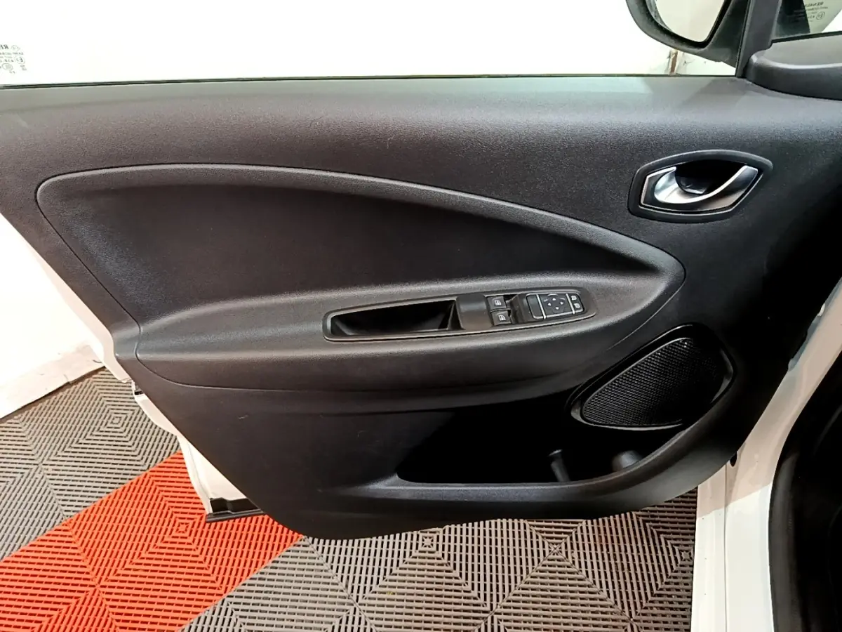 Vue rapprochée de la porte avant gauche noire de la Renault ZOE Business R110 blanche, avec commandes de vitres et haut-parleur intégré.