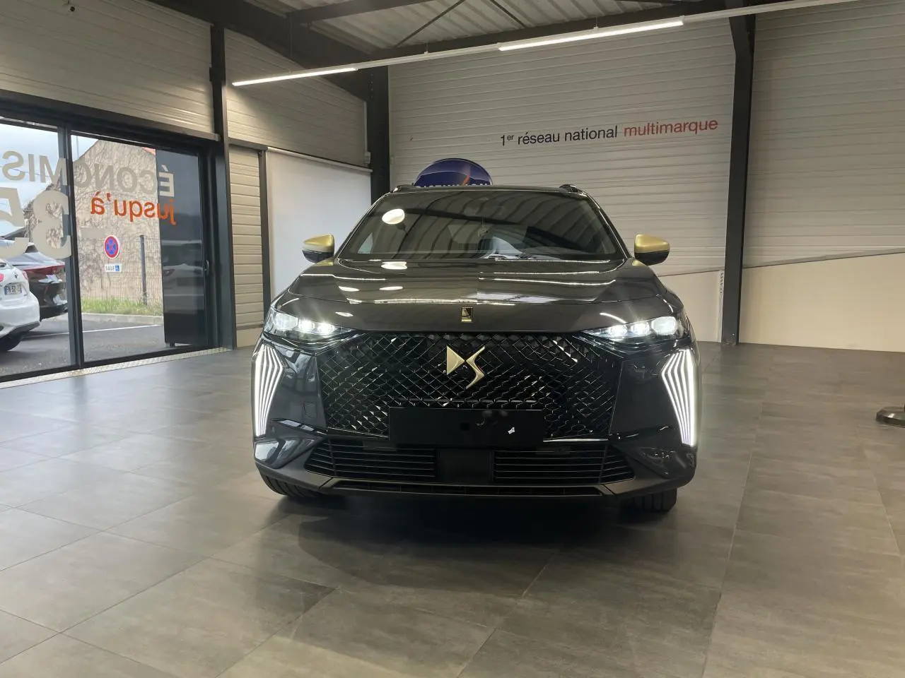 Vue de face du DS7 Crossback gris titanium avec calandre noire brillante et feux LED verticaux allumés en showroom.