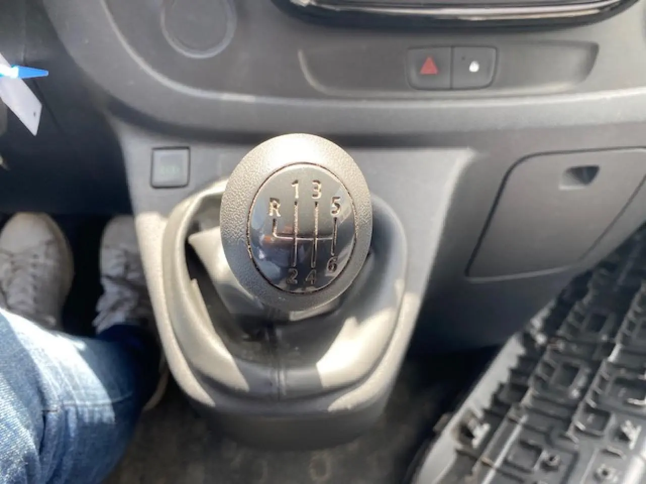 Gros plan sur le levier de vitesses manuel noir de l'Opel Vivaro blanc, avec tableau de bord gris en arrière-plan.